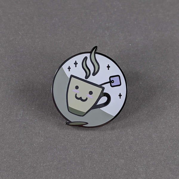 The xaichai enamel pin depicts a cute coffee mug with chai teabag hanging out. The mug is hella kawaii and smiling with rosey cheeks.