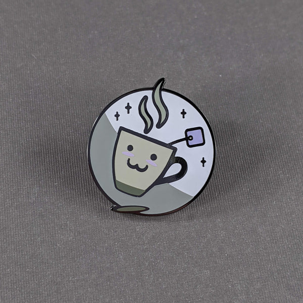The xaichai enamel pin depicts a cute coffee mug with chai teabag hanging out. The mug is hella kawaii and smiling with rosey cheeks. 